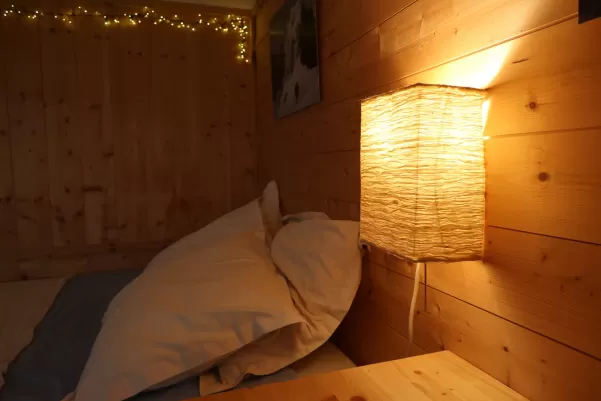 Détail du lit avec sa lampe de chevet et mur bardé de bois